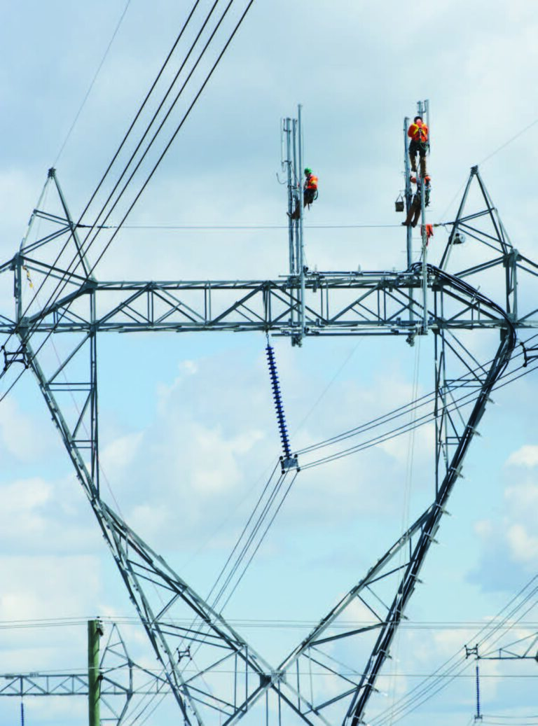 Crews installing cellular carrier antennas on the top of a high voltage lattice transmission tower