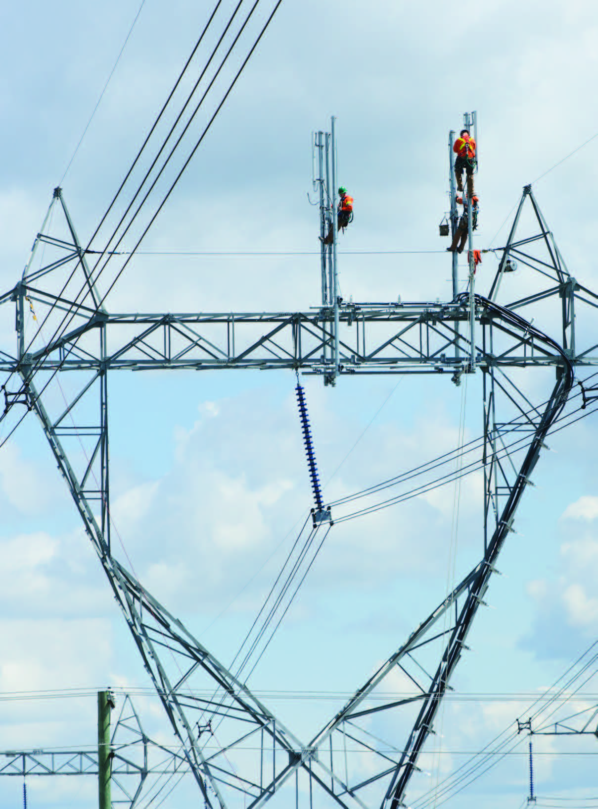 Crews installing cellular carrier antennas on the top of a high voltage lattice transmission tower
