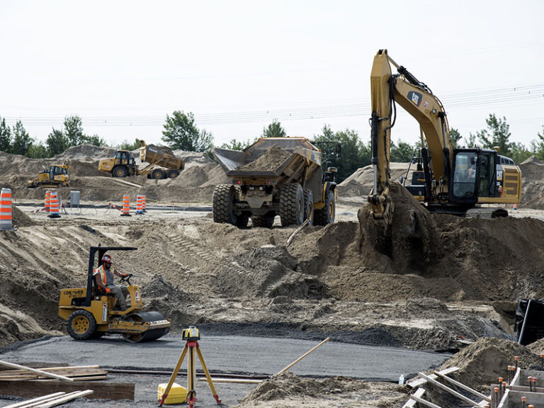 Bulk earthworks in progress with excavator, articulated dump truck, compaction roller and survey instrument