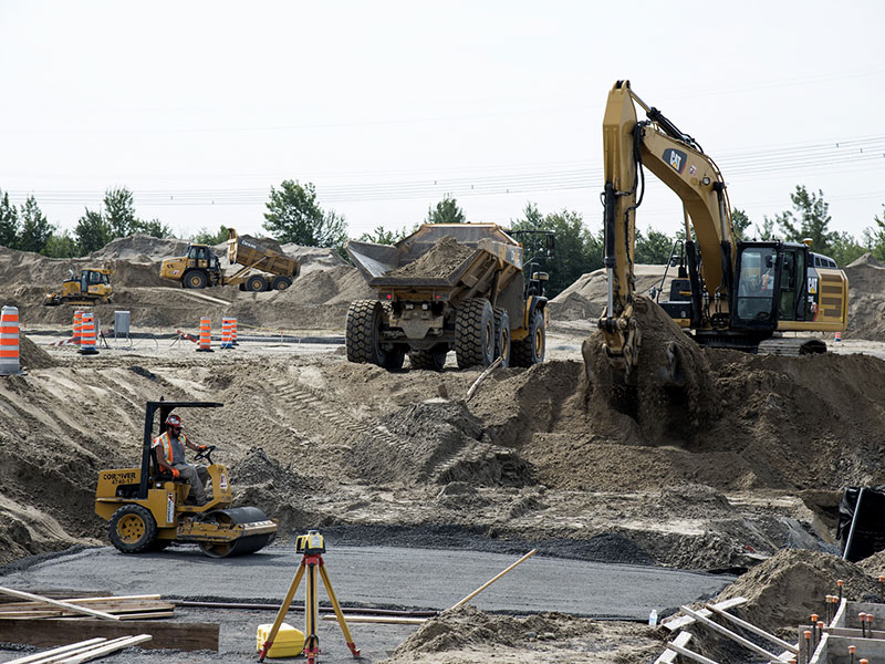 Bulk earthworks in progress with excavator, articulated dump truck, compaction roller and survey instrument
