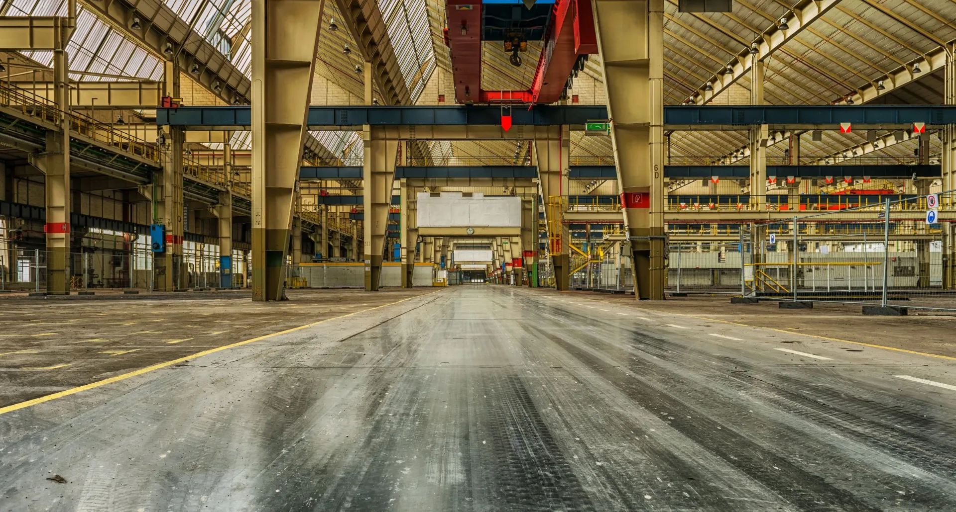 Interior of a large industrial hangar with steel roof trusses and an overhead gantry crane