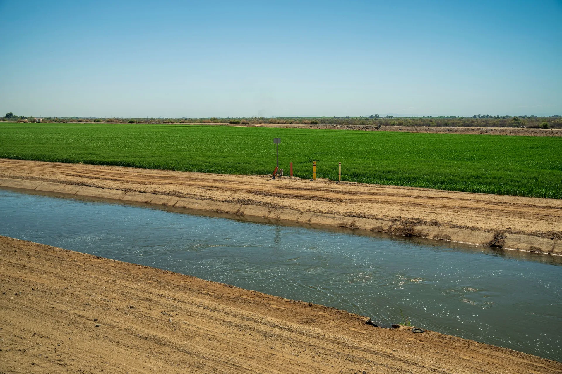 Lined irrigation canal carrying water alongside cultivated farmland