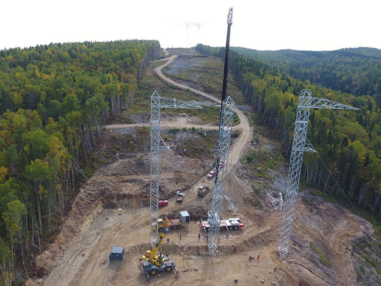 Aerial view of lattice transmission tower erection along a cleared forest right of way