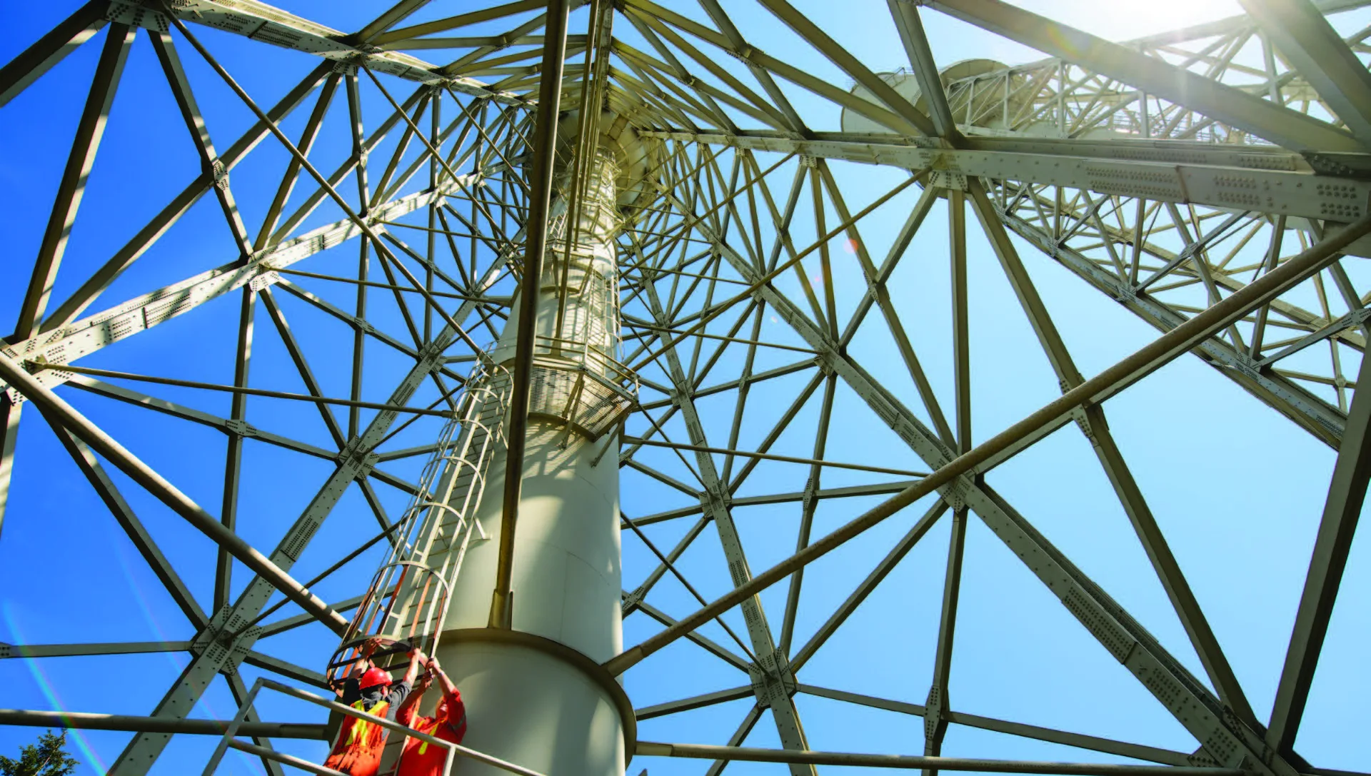 Technicians climbing the internal ladder of a large galvanised lattice tower structure