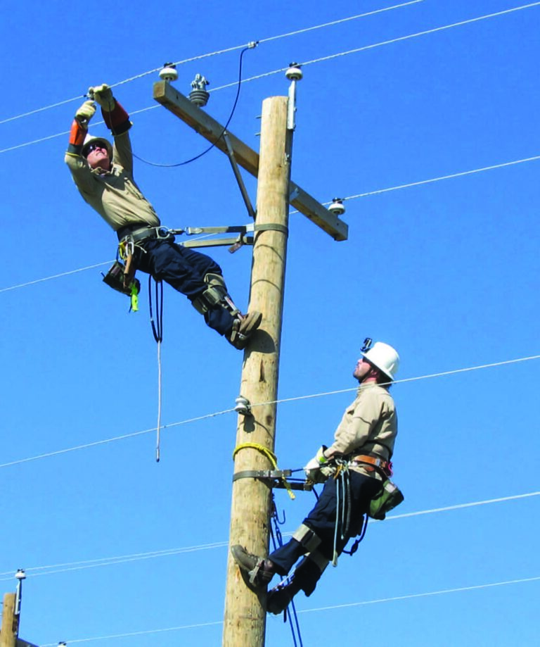 Two linemen working aloft on a wood distribution pole carrying out conductor work