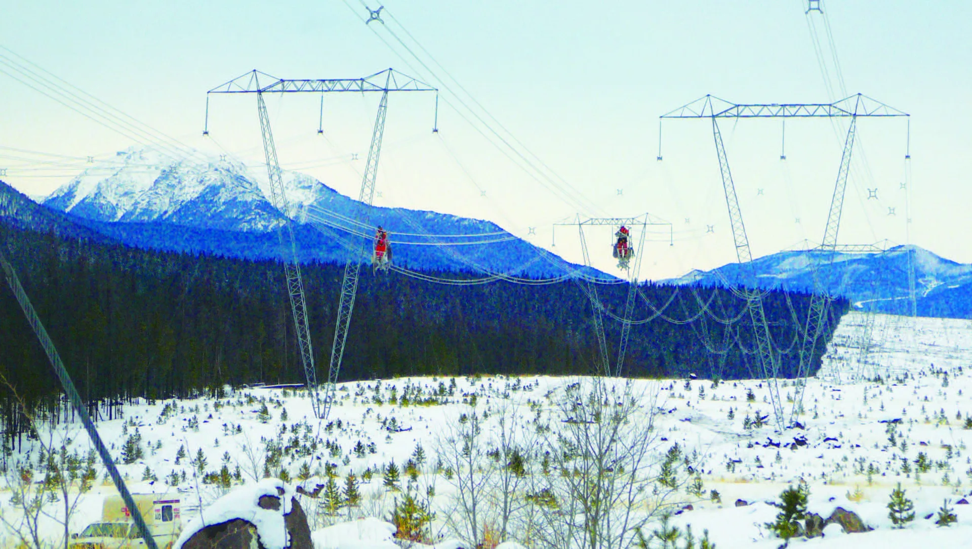 Line crews working on conductors between transmission towers in a snow covered mountain right of way