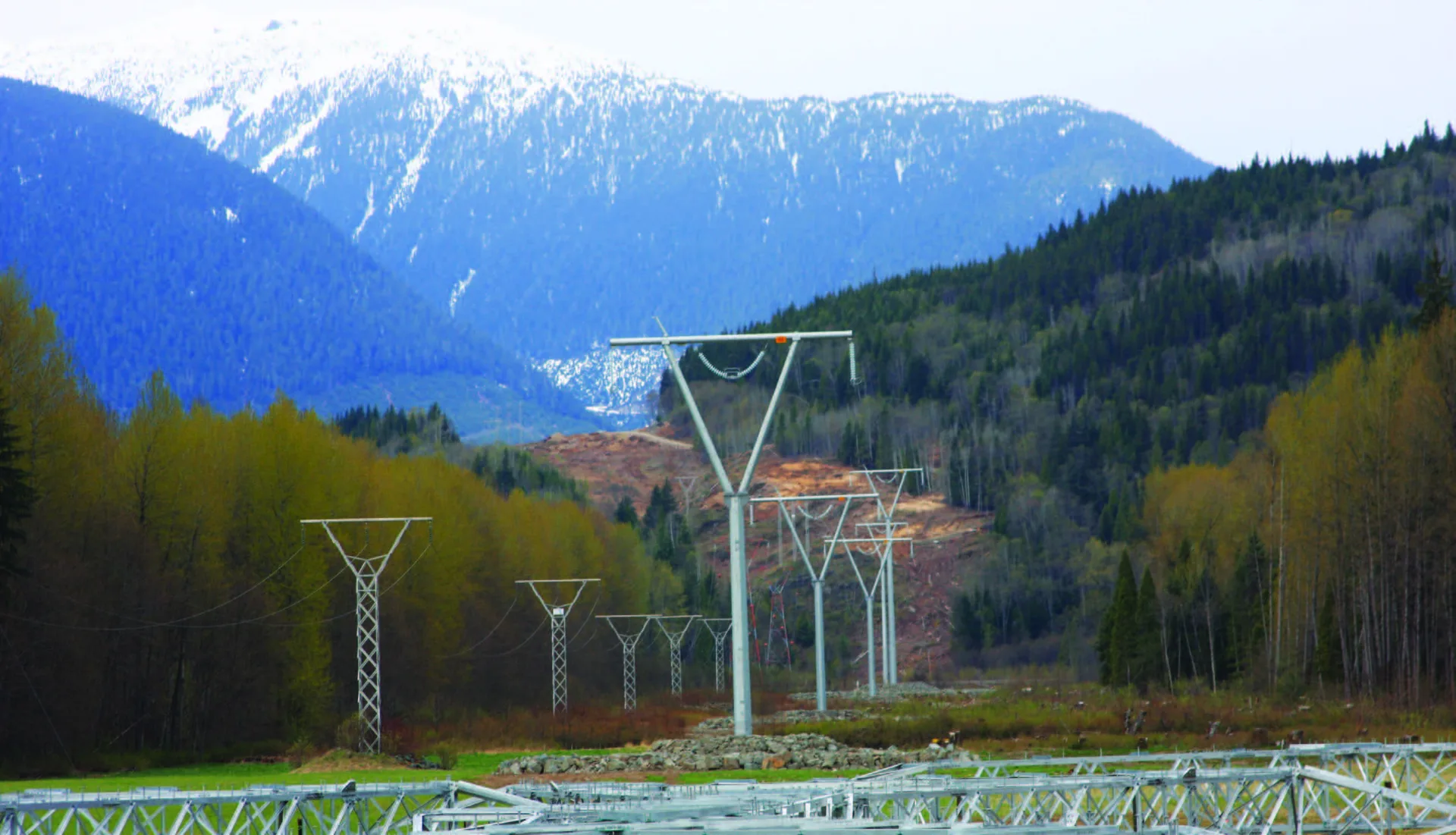 Newly constructed steel pole transmission line running through a forested mountain valley