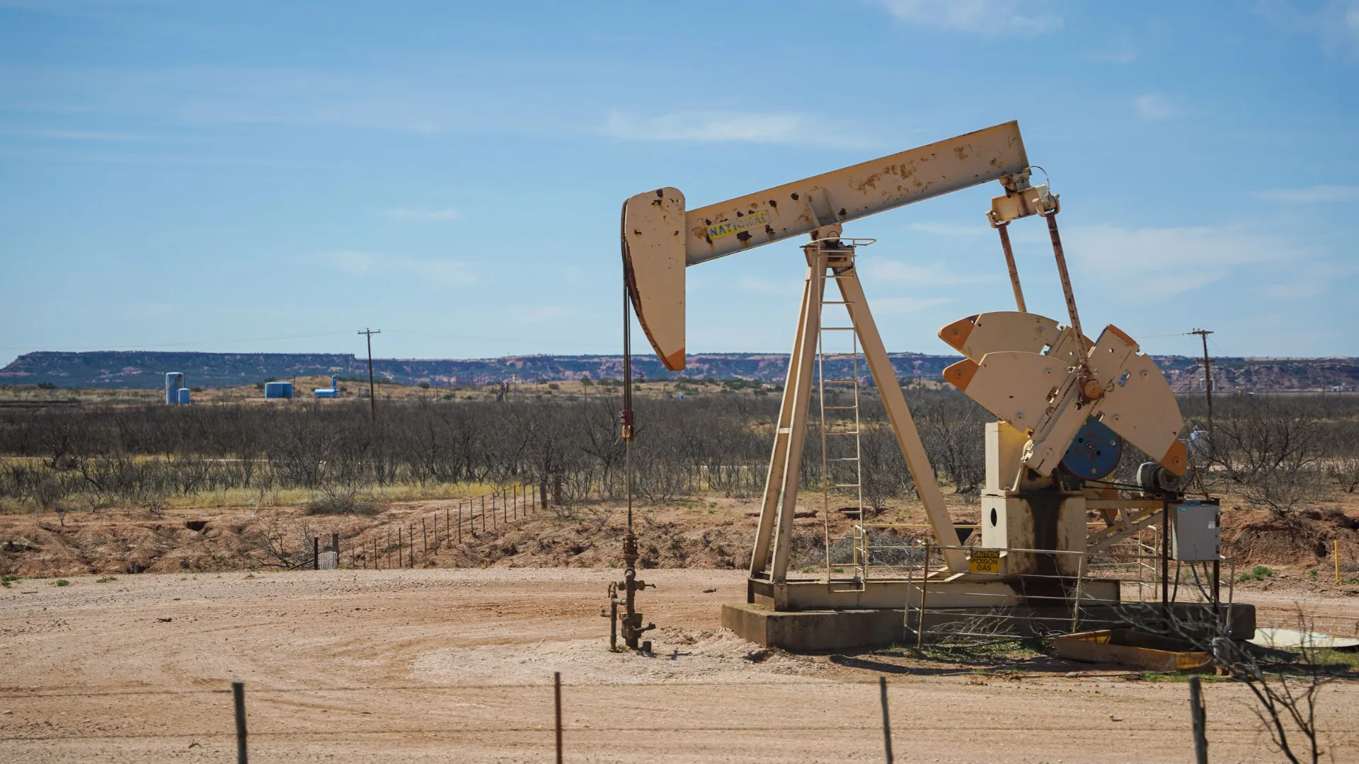 Oil well pumping unit on a remote arid plain under a blue sky