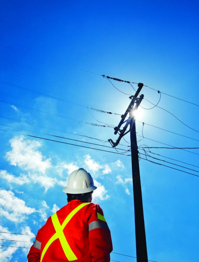 Utility worker in high visibility clothing looking up at an overhead distribution pole