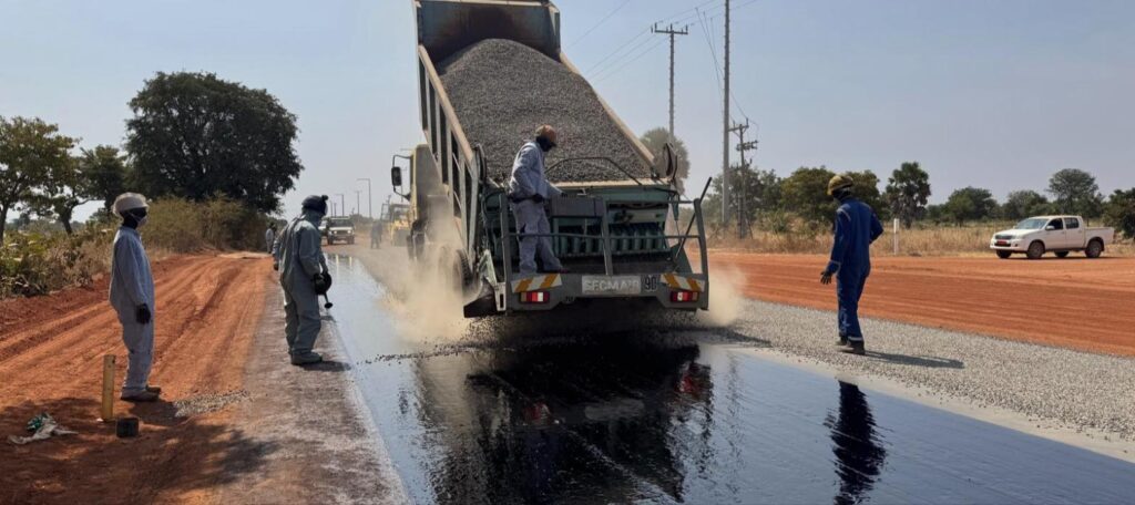 Chip spreader applying aggregate over sprayed bitumen on the Kome 4 to Madjo road, Chad