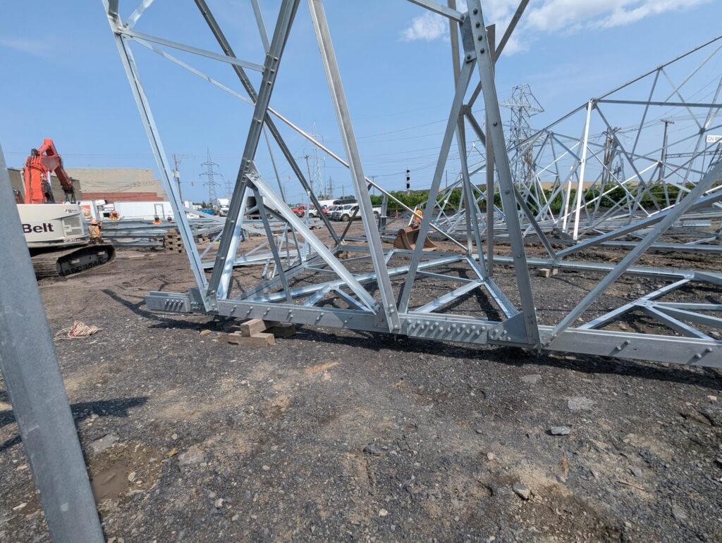 Lattice steel tower sections being assembled on site with a crawler crane in the background